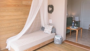 A cozy room with a wooden floor, a bed with a canopy, a small table with a bottle and glasses, and a wicker basket with magazines. - Holiday Apartment 'Suite Arte y Dragos' with Mountain View, Wi-Fi and Air Conditioning (San Bartolomé)