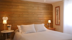 A bedroom with a wooden headboard, two bedside lamps, a framed picture on the wall, and a bedside table with a vase of flowers. - Holiday Apartment 'Suite Arte y Dragos' with Mountain View, Wi-Fi and Air Conditioning (San Bartolomé)