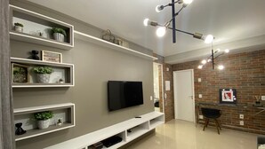 Un soggiorno moderno con televisore a schermo piatto, scaffali a muro, tavolino in legno e parete decorativa in mattoni.