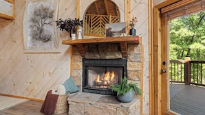 A stone fireplace with a fire, a wooden shelf with decorative items, a framed picture, and a view of the outdoors. - Gated Resort Setting*WiFi*Spacious*Hot Tub (Sevierville)