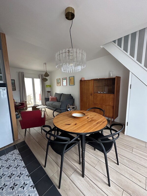 A dining area with a round wooden table, black chairs, and a hanging crystal chandelier.