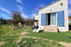 A modern house with a white exterior, blue shutters, and a small porch with two lounge chairs.
