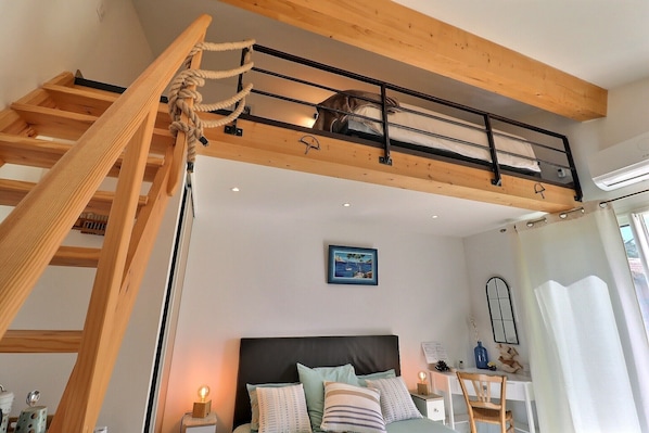 A loft-style bedroom with a wooden ladder, a bunk bed, a desk, and a nightstand.