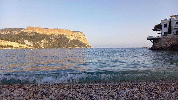 Eine Küstenlandschaft mit einem Kiesstrand, einer Klippe und einem Gebäude mit einem Balkon mit Meerblick.