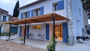 Ein zweistöckiges Haus mit überdachter Terrasse, Sitzgelegenheit im Freien und einer Steinaußenfassade.