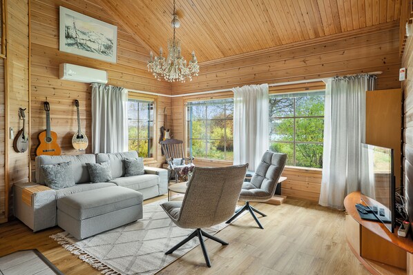 L’intérieur d’un chalet accueillant, avec un plafond en bois, un lustre, un canapé gris, un fauteuil gris et une table à manger.
