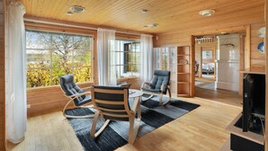 A wooden-paneled room with a dining table, two chairs, a fireplace, and large windows.