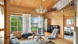A wooden cabin interior with a sofa, armchairs, a TV, and a chandelier.