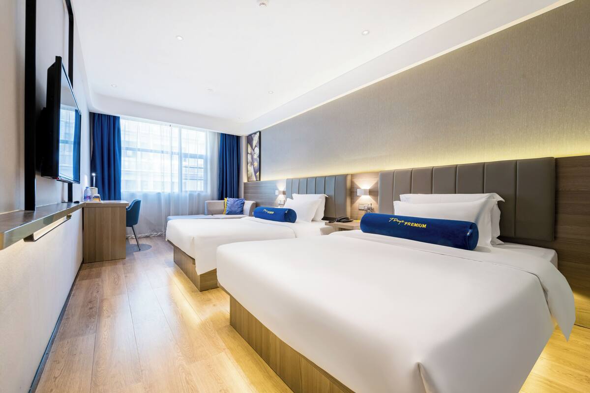 A hotel room with two beds, a desk, a flat-screen TV, and a large window with curtains.