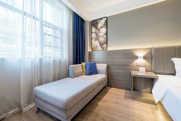 A hotel room with a bed, a sofa, a nightstand, a wall-mounted lamp, and a large window with curtains. - 7 Days Youpin Premium (Shenzhen)