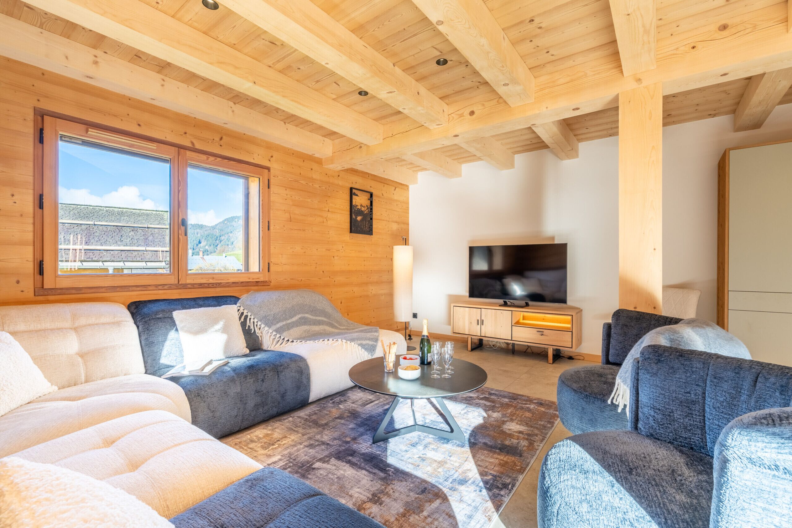 Una sala de estar acogedora con vigas de madera, un televisor grande y asientos cómodos.