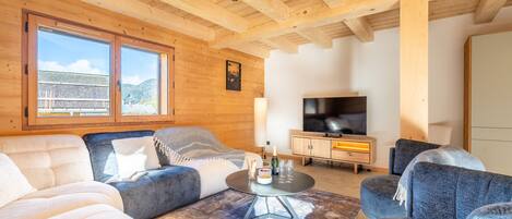Una sala de estar acogedora con vigas de madera, un televisor grande y asientos cómodos.