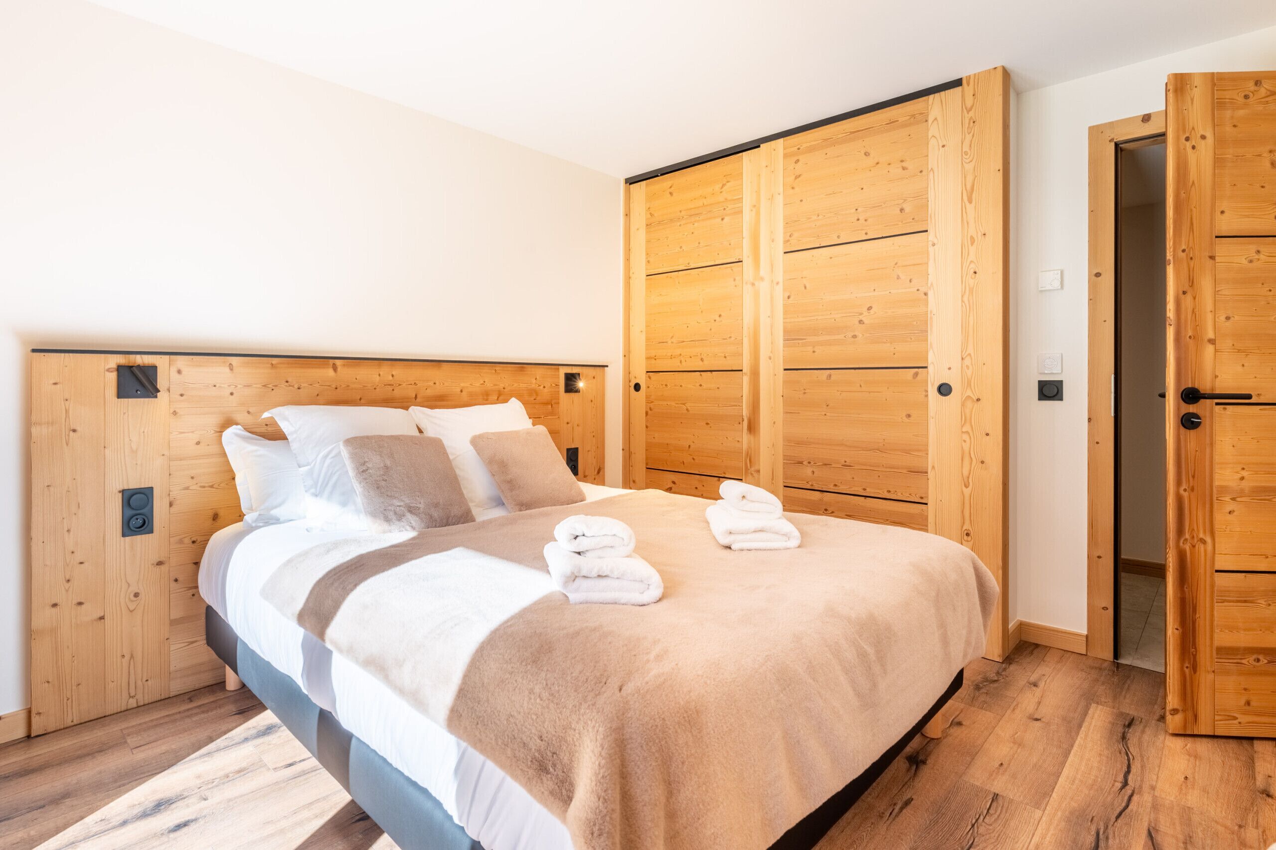 A bedroom with a wooden headboard, a bed with white and brown bedding, and a wooden wardrobe.