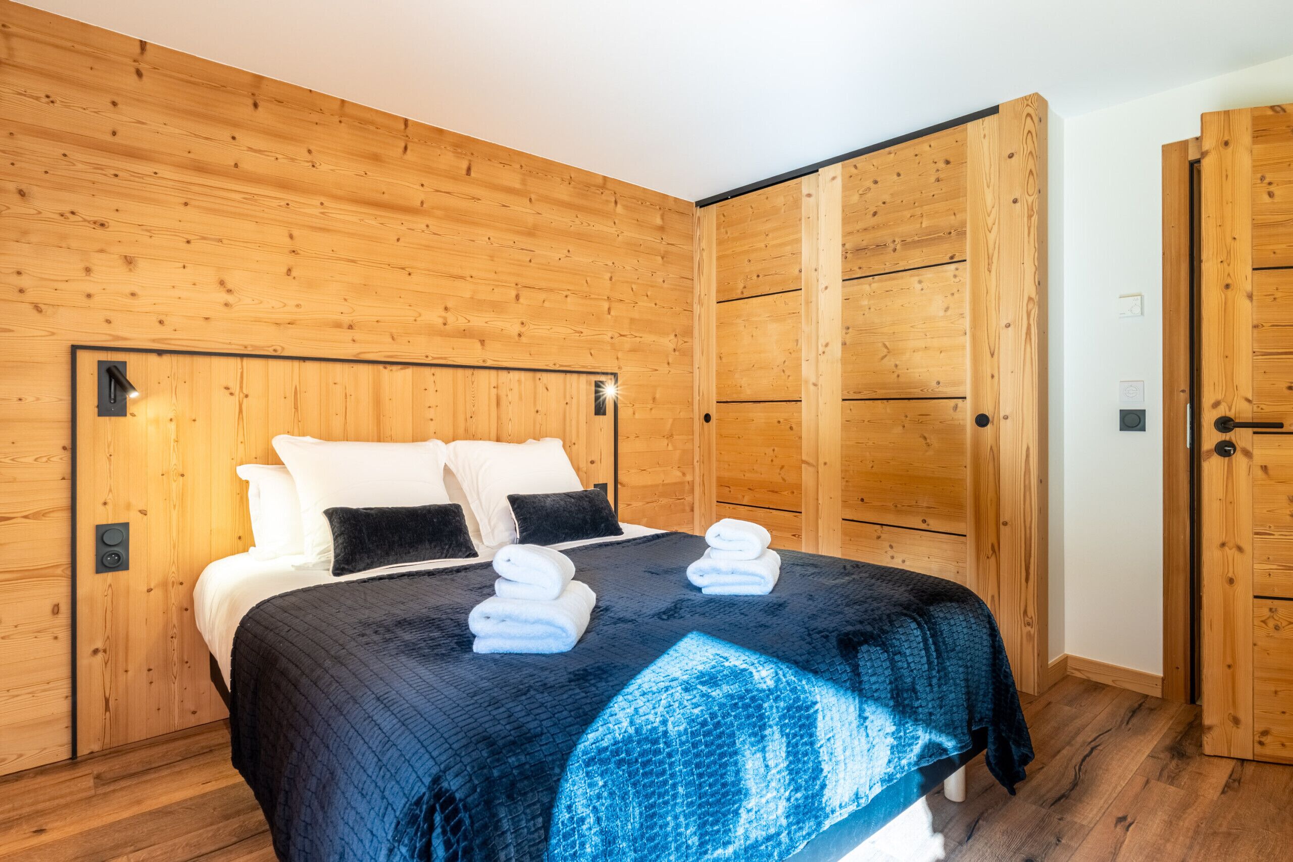 Un dormitorio con paneles de madera, una cama, almohadas y toallas dobladas con cuidado.