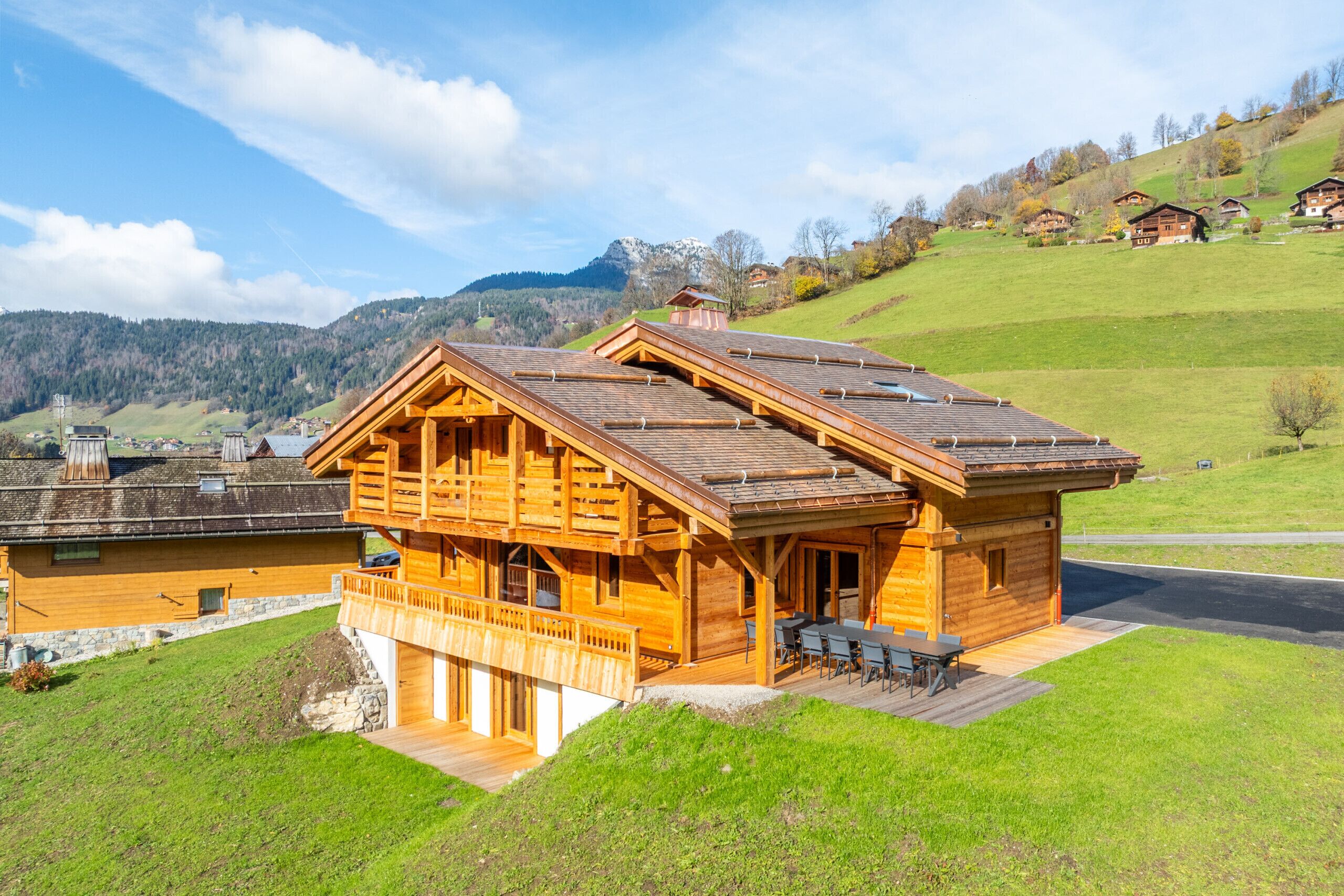 A wooden chalet with a balcony, a stone foundation, and a view of a mountain range.