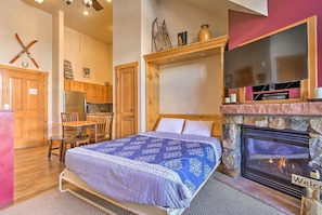 A bedroom with a bed, a fireplace, a kitchen area, and a dining table.