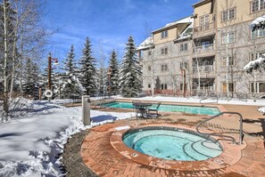 A pool area with a hot tub, surrounded by snow-covered trees and a building with balconies. - Keystone Studio Vacation Retreat,Hot tubs,pool,etc (Keystone)