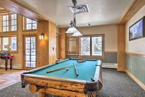 A pool table in a room with wooden walls and large windows.