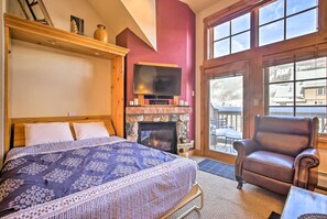 A bedroom with a bed, a fireplace, a television, and a leather chair.