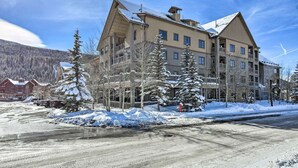 Un hôtel à plusieurs étages, avec un chalet de ski situé au dernier niveau, entouré d’arbres couverts de neige et dominant un paysage montagneux.