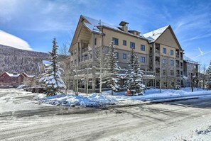 A multi-story hotel with a ski lodge on the upper level, surrounded by snow-covered trees and a mountainous backdrop.