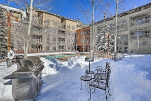 A snow-covered outdoor area with a barbecue grill, metal chairs, and a pool.