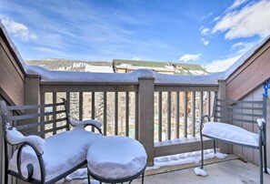 A balcony with two metal chairs covered in snow, a wooden fence, and a view of a snowy landscape with buildings in the background. - Keystone Studio Vacation Retreat,Hot tubs,pool,etc (Keystone)
