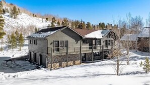 Une cabane en rondins à deux étages, avec des fondations en pierre, un balcon et un toit recouvert de neige.