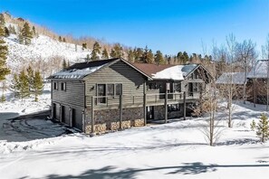 Une cabane en rondins à deux étages, avec des fondations en pierre, un balcon et un toit recouvert de neige.