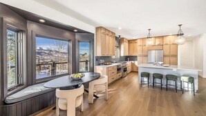 Een moderne keuken met houten kastjes, een centraal eiland met barstoelen en grote ramen met uitzicht op de bergen.