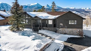 Een houten hut met een stenen fundering, omringd door een met sneeuw bedekte grond en een bergachtige achtergrond.
