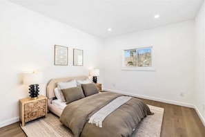 A bedroom with a bed, two bedside tables, a window, and two framed pictures on the wall.