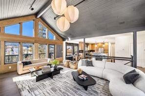 Ein großzügiger Wohnbereich mit einer großen Couch, einem Couchtisch und Blick auf die Küche und den Essbereich durch große Fenster.