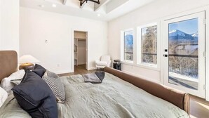 Een slaapkamer met een bed, een stoel, een bureau en een groot raam met uitzicht op bergen.
