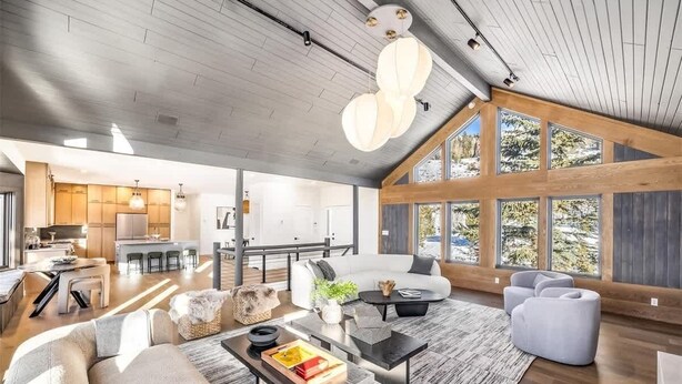 Een ruime woonkamer met een hoge plafond, modern meubilair en grote ramen met uitzicht op de omgeving.
