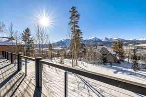 Eine Holzterrasse mit Metallgeländer, die auf eine verschneite Landschaft mit Bergen im Hintergrund blickt.