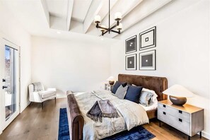 Une chambre à coucher moderne avec un grand lit, des tables de chevet, un lustre et des tableaux encadrés accrochés au mur.