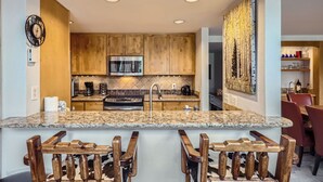 A modern kitchen with wooden cabinets, a built-in microwave, a stove, and a large island with bar stools. - Keystone MTN Haven! (Keystone)