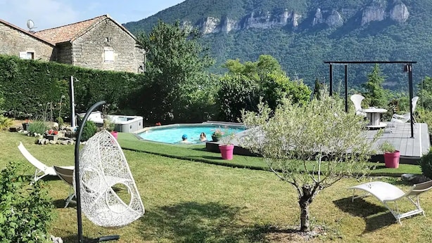 A pool area with a mountain backdrop, a stone building, and outdoor seating. - Guest Rooms – Château at lesoleilo.com with Shared Pool from 12/06 to 13/09/2026 (Mostuéjouls)