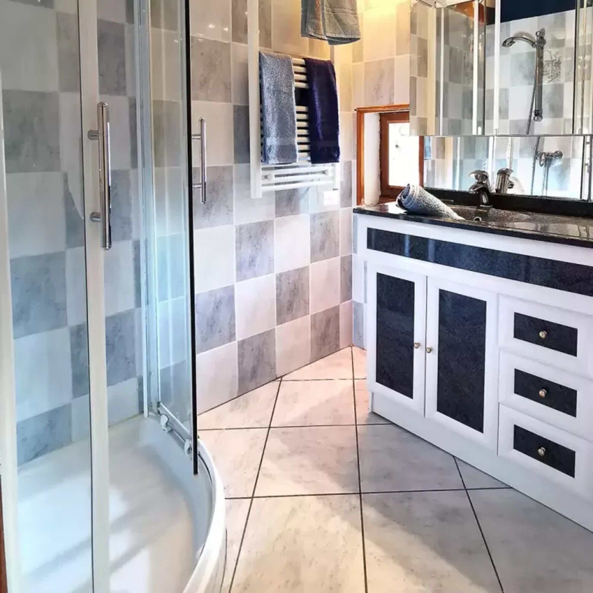 Une salle de bain avec une douche à parois de verre, un carrelage au sol, un lavabo avec un miroir et un porte-serviettes.