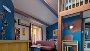 A loft-style room with a high ceiling, a wooden staircase, a red sofa, a small table, and a suitcase. - Guest Rooms – Château at lesoleilo.com with Shared Pool from 12/06 to 13/09/2026 (Mostuéjouls)