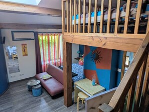A loft-style room with a wooden staircase, a sofa, a small table, and a colorful wall decoration. - Guest Rooms – Château at lesoleilo.com with Shared Pool from 12/06 to 13/09/2026 (Mostuéjouls)