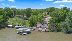 A riverside property with docked boats, a house with a covered patio, and lush greenery. - Winding Bay - Lakefront with stellar main channel views! (Sunrise Beach)
