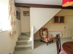 A staircase leading to a landing with a patterned armchair and a wooden chair. - The Gameskeepers Cottage (Grange-over-Sands)