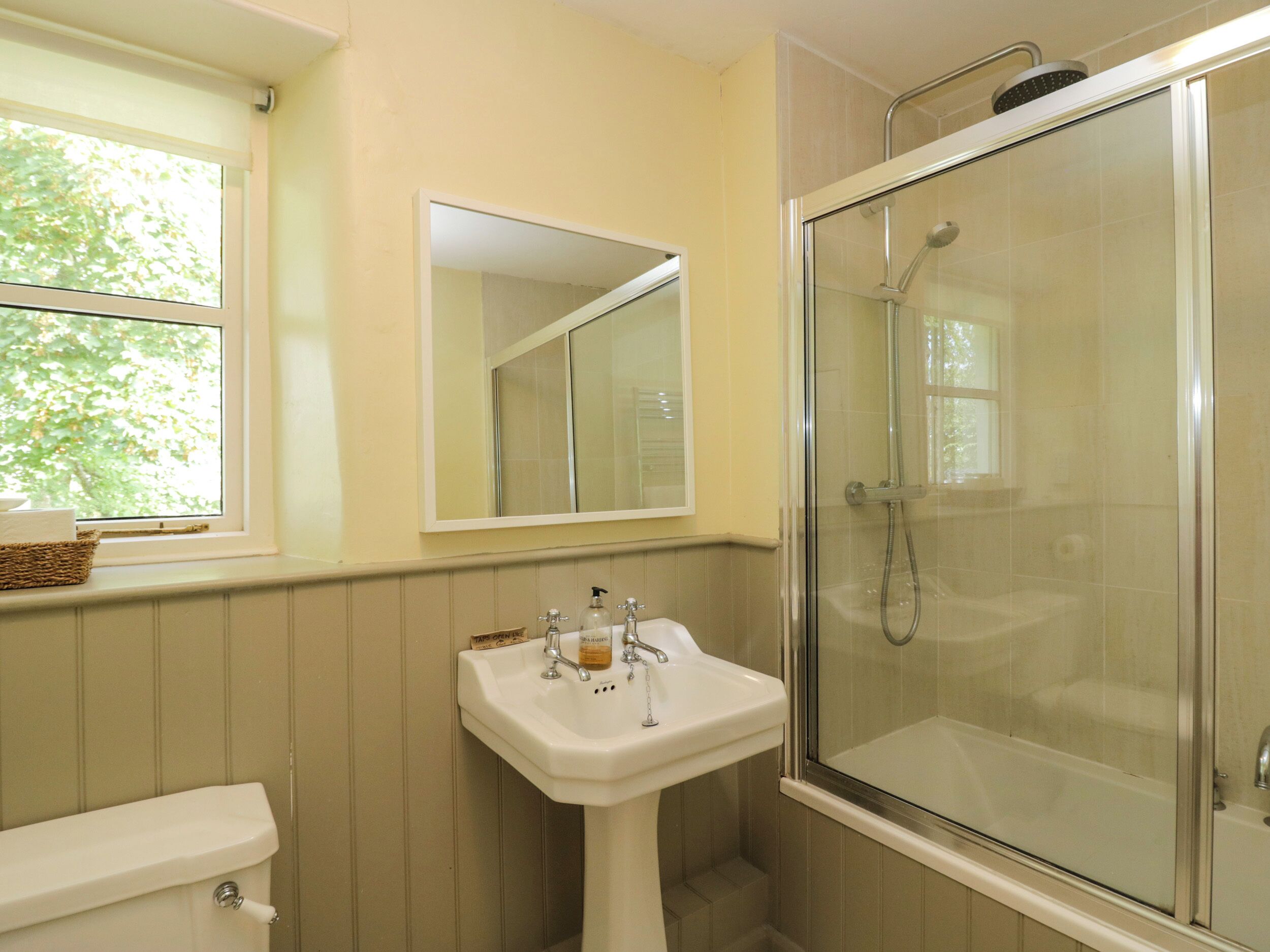 A bathroom with a toilet, a sink, a mirror, and a glass-enclosed shower.