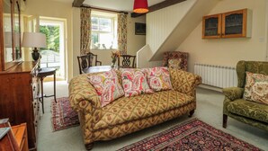 A cozy living room with a patterned sofa, a dining table, and a staircase leading to an upper level. - The Gameskeepers Cottage (Grange-over-Sands)