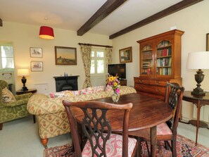 A traditional living room with a wooden dining table, chairs, a fireplace, a television, and a bookshelf. - The Gameskeepers Cottage (Grange-over-Sands)