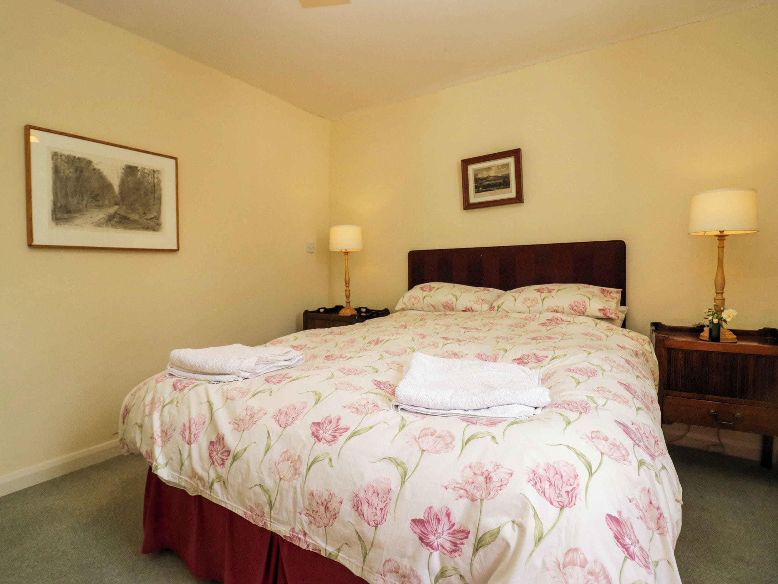 A neatly made bed with floral bedding, two bedside tables with lamps, and a framed picture on the wall.