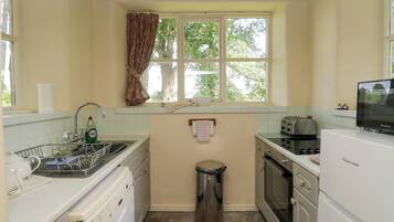 A compact kitchen with a sink, a washing machine, a trash bin, and a toaster.