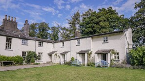A traditional white building with multiple windows and doors, surrounded by a well-maintained lawn and trees. - The Gameskeepers Cottage (Grange-over-Sands)